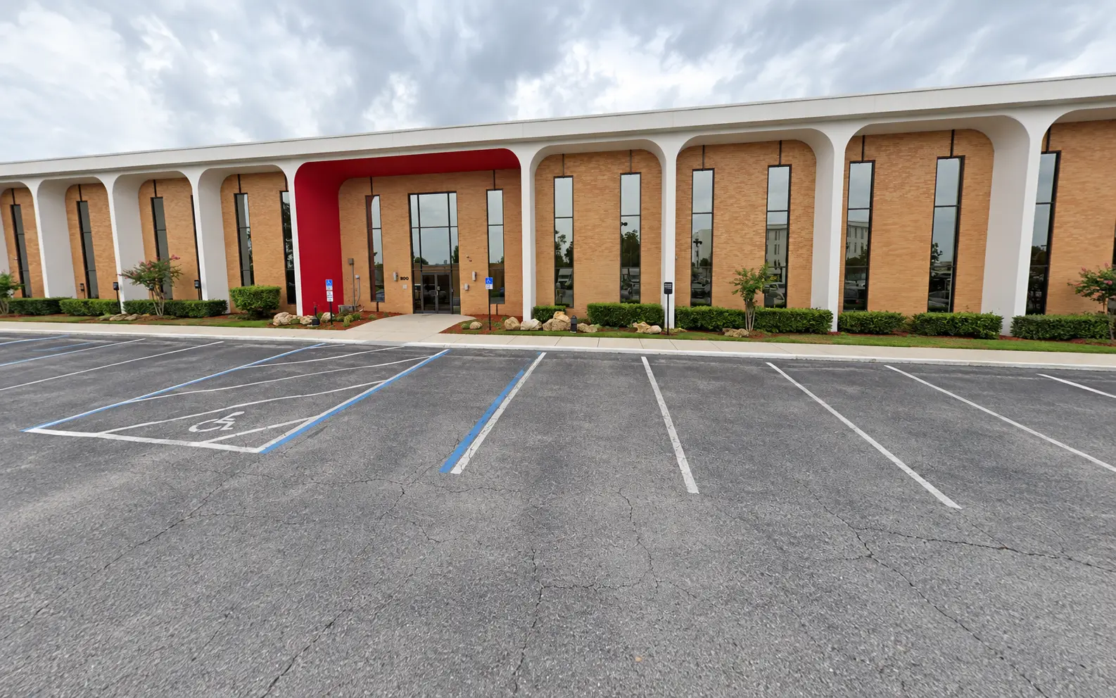 The Jude Health Institute building on Lake Ellenor Drive, Orlando — a single-storey brick building with white arches and a red entrance surround, with parking immediately outside the doors